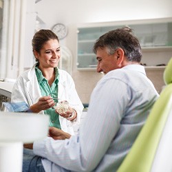 Smiling dentist showing patient model of teeth