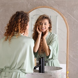 a smiling woman looking in her bathroom mirror