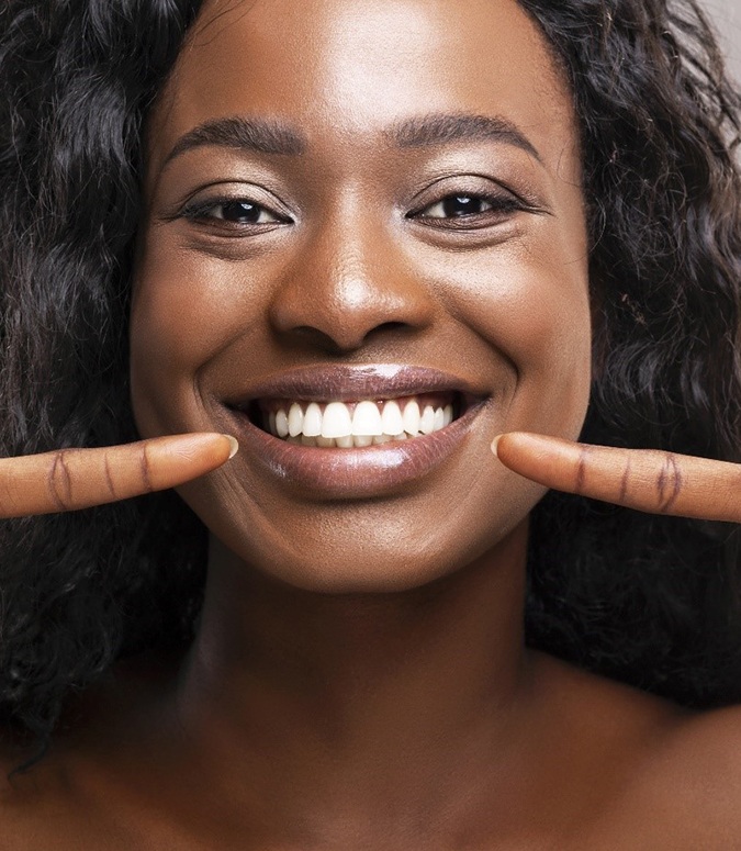 Happy woman pointing at her perfect teeth after visiting cosmetic dentist