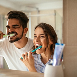 A man and woman brushing their teeth in front of a bathroom mirror