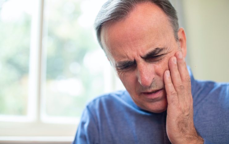 Man in need of restorative dentistry holding his cheek