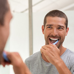 Man smiling while brushing his teeth in bathroom