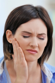 Woman in need of restorative dentistry holding cheek in pain