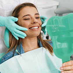 woman smiling while holding dental mirror 